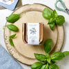 Sweet Basil in a copper tin, sitting on top of a chopping board with some cut herbs.