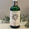 A green glass spray bottle with a white label featuring a hand-drawn design of a bundle of herbs.
