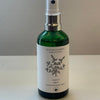 A green glass spray bottle with a white label featuring a hand-drawn design of a bundle of herbs.