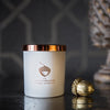 A matte-white container with a shiny copper lid sits on a black table against a dark background.