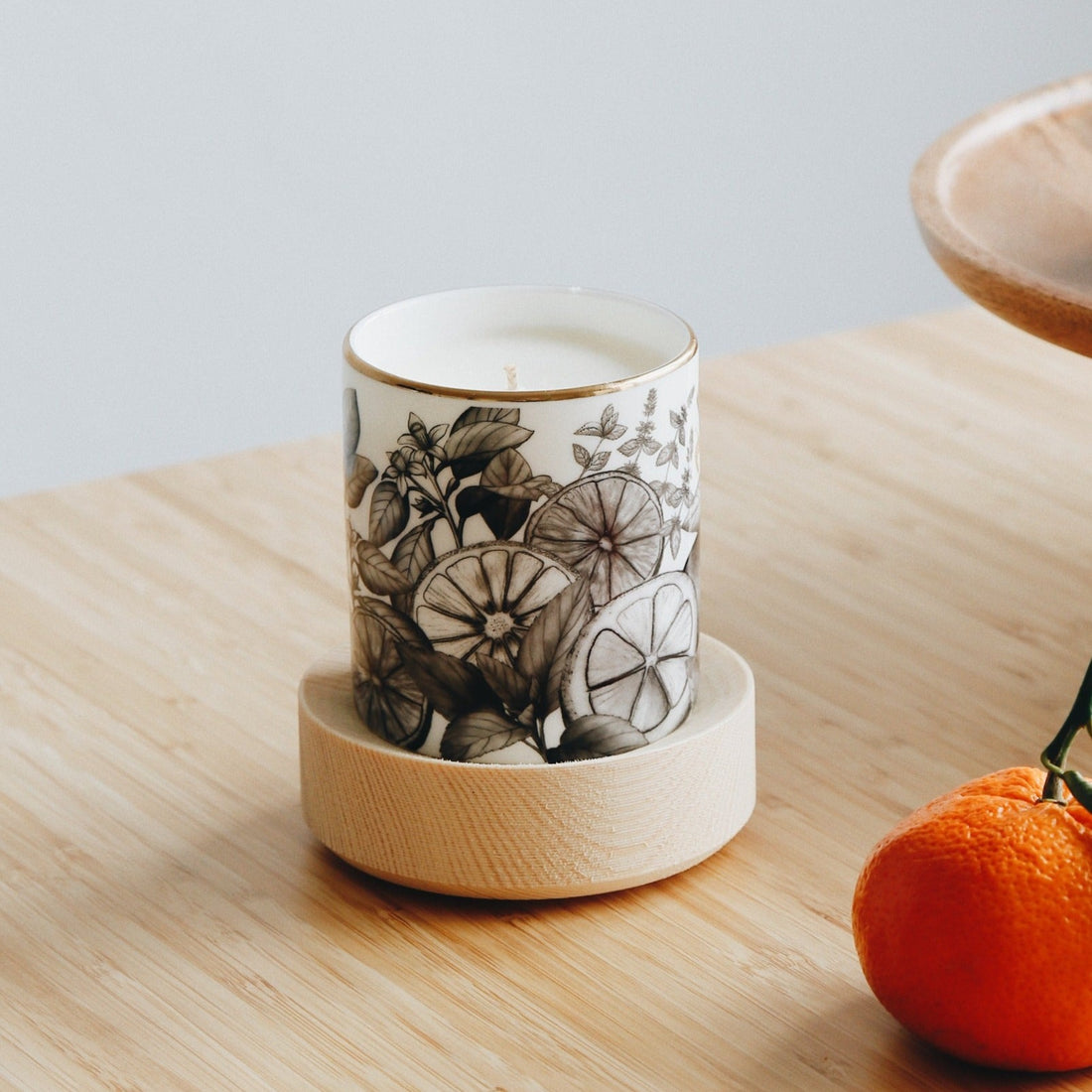  Create candle in a Bone China container printed with a hand-drawn illustration of the plants used in the fragrance, including lemon, orange, and spearmint. Around the rim is a stripe of shiny 24k gold. Placed around the candle are fresh oranges.