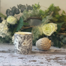  Bliss candle in a Bone China container printed with a hand-drawn illustration of the plants used in the fragrance, including jasmine, ylang-ylang, & cardamom. Around the rim is a stripe of shiny 24k gold.
