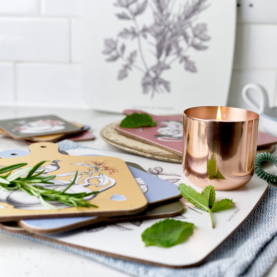 Rosemary & Coriander in a copper tin, sitting on top of a chopping board with some cut herbs.
