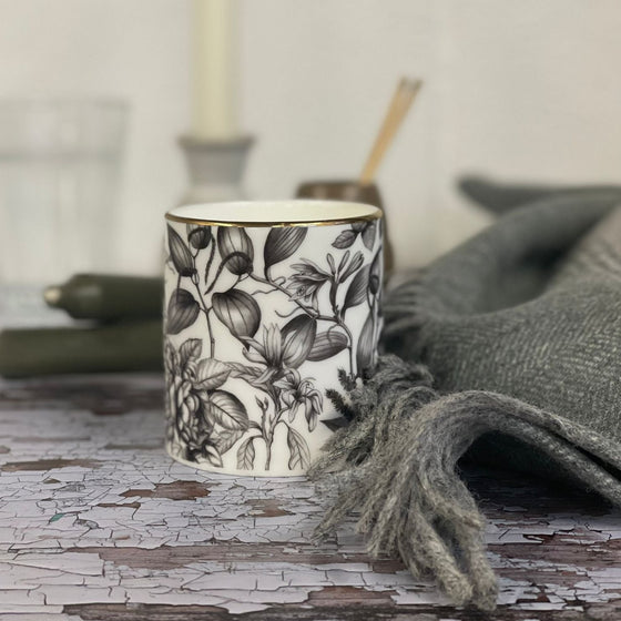 Sensual candle in a Bone China container printed with a hand-drawn illustration of the plants used in the fragrance, including patchouli, rose, and black pepper. Around the rim is a stripe of shiny 24k gold.