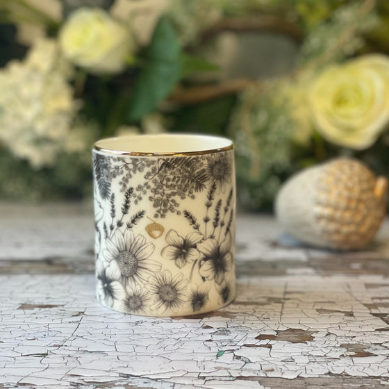 Affirmation candle in a Bone China container printed with a hand-drawn illustration of the plants used in the fragrance, including violet, lavender, & chamomile.. Around the rim is a stripe of shiny 24k gold.