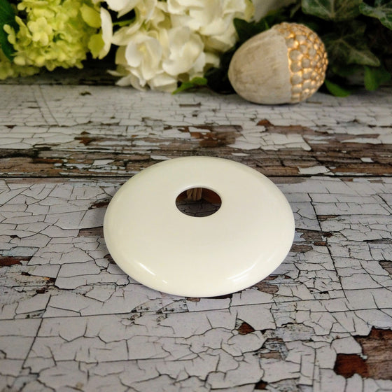 The bone china lid sits on a wooden surface. It is white, with a hole in the middle to put reeds in.