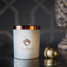  Matte-white candle with a shiny copper lid sits on a black table against a black background.