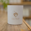 A close-up image of the Bliss candle in a matte-white container with copper acorn logo.
