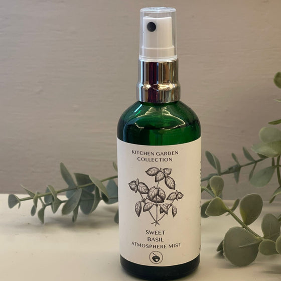 A green glass spray bottle with a white label featuring a hand-drawn design of a bundle of herbs.
